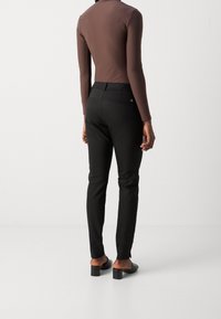 Hnědý body s dlouhým rukávem v kombinaci s černými klasickými kalhotami, které mají slim fit, minimální detaily a černé podpatky na světlém pozadí.