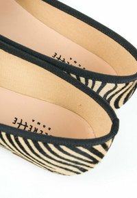 Scarpe slip-on a stampa zebra nera e beige con parte superiore in tessuto morbido e rifiniture nere lungo l'apertura, dotate di una soletta liscia color nocciola.