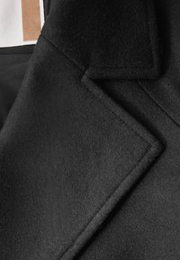 Czarny wełniany płaszcz z wyłamią kołnierza, prostym krojem i miękką fakturą. Wyraźny detal w postaci ściegów na krawędzi ko�łnierza.