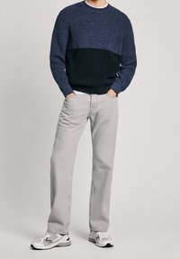 Marinblå och mörkblå stickad tröja med ribbad nederkant, kombinerad med ljusgrå raka jeans och vita sneakers med svarta detaljer.