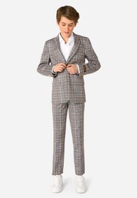 Completo a scacchi grigio con un blazer con rever a punta e bottoni oro, abbinato a pantaloni coordinati e sneakers bianche.