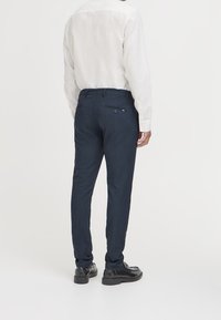 Námořnické modré oblekové kalhoty, slim fit, se zadními kapsami a uzavíráním na knoflík. V kombinaci s dlouhým světle zbarveným tričkem s dlouhým rukávem.