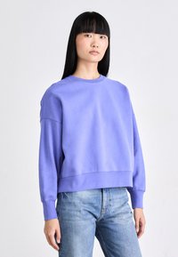 Sudadera morada recortada con cuello redondo y mangas largas, hecha de una tela suave, combinada con jeans de color azul claro.