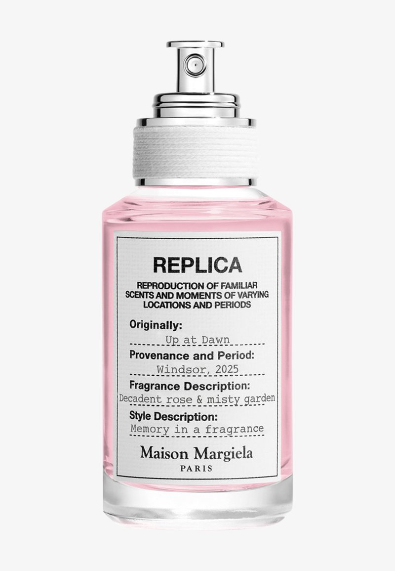Flacon de parfum Maison Margiela Replica avec liquide rose, pulvérisateur argenté, étiquette indiquant le parfum "Up at Dawn" avec des notes de rose et de jardin embrumé.