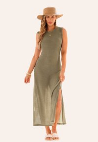 Vestito maxi senza maniche di colore verde oliva con un design a nido d'ape testurizzato e uno spacco alto fino alla coscia, abbinato a un cappello di paglia e sandali bianchi.