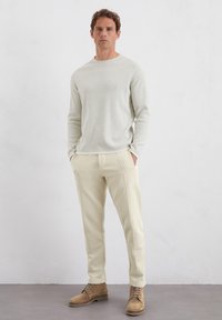 Lichtgrijze gebreide trui, roomkleurige broek met naaddetails en tan kleurige veterschoenen. Eenvoudig, gestroomlijnd ontwerp met neutrale kleuren.