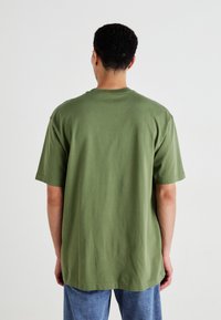 Grøn bomulds T-shirt, løstsiddende, korte ærmer, rund halsudskæring, glat struktur, synlige sømdetaljer, båret med blå denimjeans.