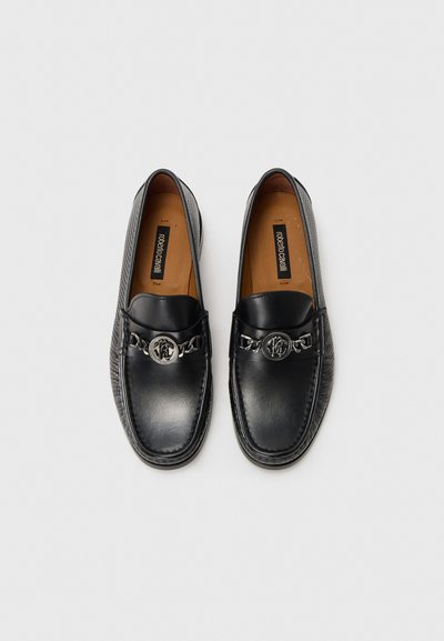 Schwarze Lederloafers mit glänzender Textur, versehen mit einem silbernen Kettenakzent und Logo-Detail auf der Schnalle, runder Zehenform und beigem Innenfutter.