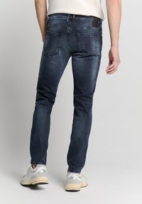 Donkerblauwe denim jeans met een slim fit, met een gladde textuur, vijf zakken en een zwart logo patch op de achterste tailleband.