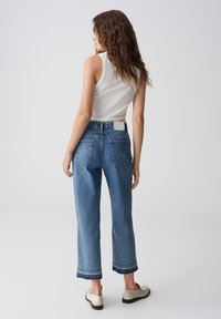 Jeans a vita alta blu con taglio dritto, caratterizzati da un orlo grezzo, tasche posteriori e una texture di denim di lavaggio chiaro.