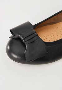 Zwarte leren ballerina met een gestructureerde afwerking, voorzien van een grote strikaccent op de neus en een gewatteerde binnenzool met perforaties.