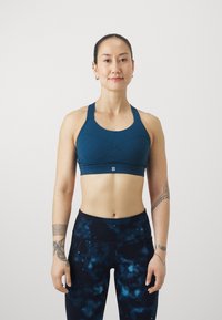 Tirkīza sporta krūšturis ar sacensību muguru un krustu šuvēm. Apvienots ar augsto jostasvietu tumši zilām legingām ar galaktikas druku.