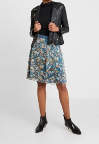 Sorte læderbikerjakke over en mørk bluse, parret med en blomsterprint, knælang nederdel i blå, der har forskellige farver og en tætsiddende talje. Sorte ankelstøvler med hæl fuldender outfittet.