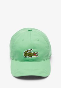 Gorra de béisbol verde hecha de algodón, con un logo bordado de cocodrilo en la parte frontal en verde con acentos rojos. Visera plana y parte trasera ajustable.