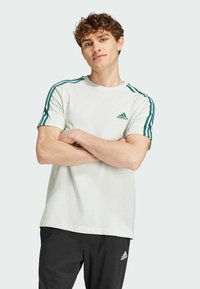 Maglietta di cotone verde chiaro a maniche corte, con strisce verde scuro sulle spalle e un logo ricamato sul petto.