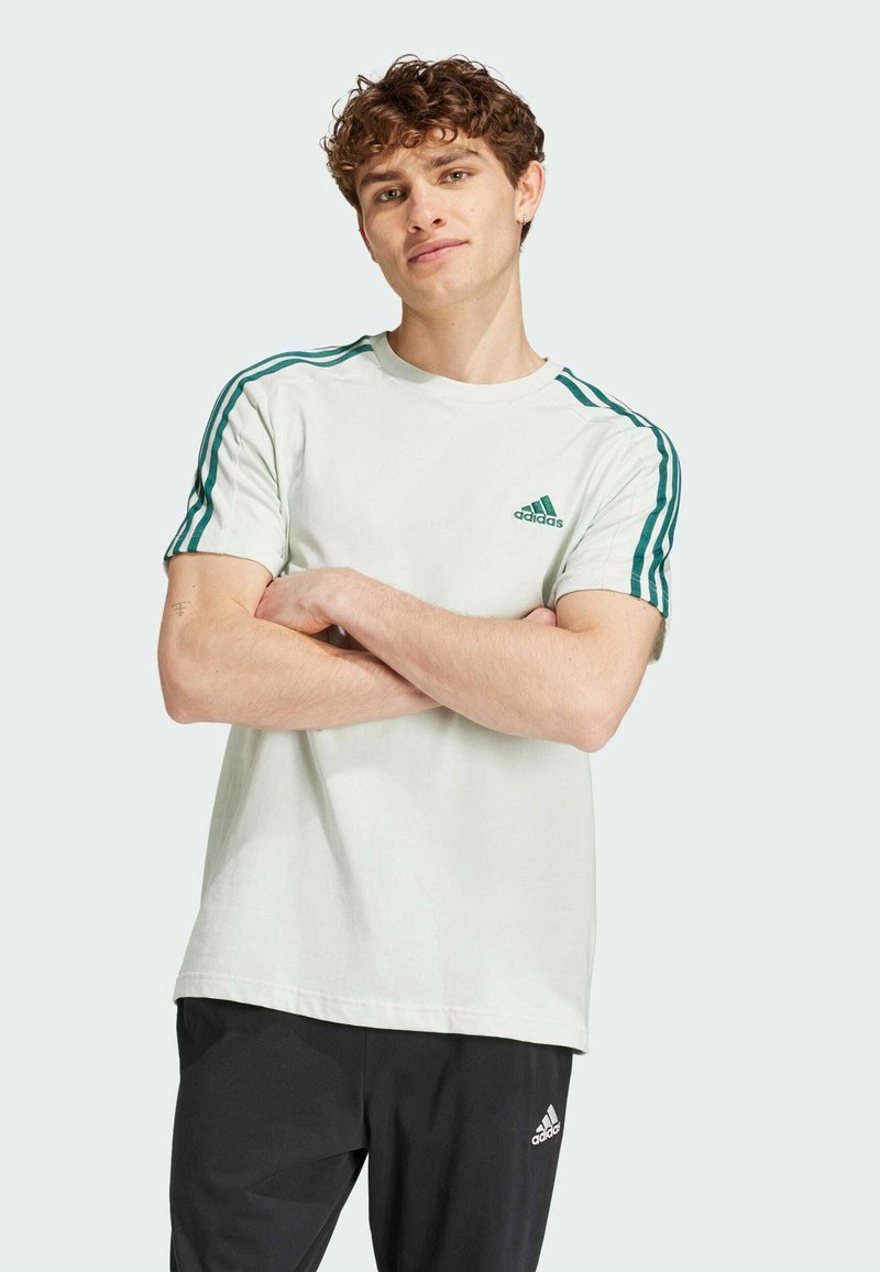 Maglietta di cotone verde chiaro a maniche corte, con strisce verde scuro sulle spalle e un logo ricamato sul petto.