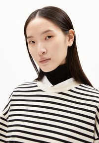 Maglione a righe bianche e nere con colletto ampio, abbinato a un dolcevita nero. Tessuto morbido con vestibilità rilassata, dettagli minimali.