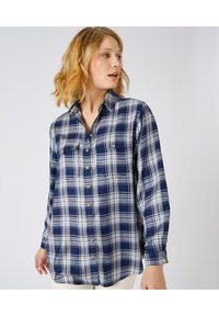 Camicia a quadri blu navy in cotone, con motivo a quadri bianchi, chiusura con bottoni frontale, due tasche sul petto e maniche lunghe con polsini a bottoni.