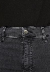 Mörkgrå denimjeans med en slät yta, utrustade med en silverfärgad metallknapp, hällor för bälte och synliga sömmar längs midjebandet.