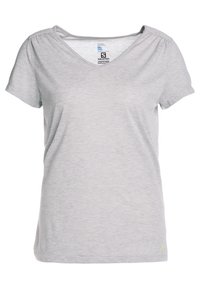 Světle šedé tričko s krátkým rukávem a výstřihem do V, s jemnou texturou. Má nařasené švy na ramenou a malé logo v dolním rohu.