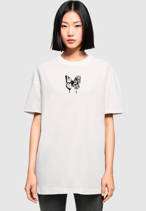 Hvid bomulds t-shirt med korte ærmer, der har et sort sommerfugle- og blomsterdesign på fronten. Løs pasform, rund hals.