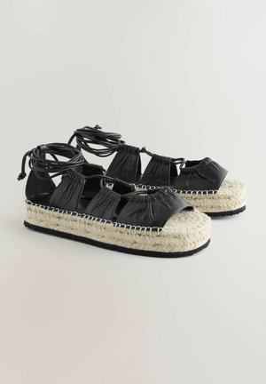 Sandali espadrille in pelle nera con suola in juta intrecciata, lacci regolabili e design open toe. Presentano una finitura texturizzata e dettagli cuciti.