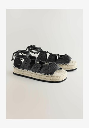 Sandali espadrille in pelle nera con suola in juta intrecciata, lacci regolabili e design open toe. Presentano una finitura texturizzata e dettagli cuciti.