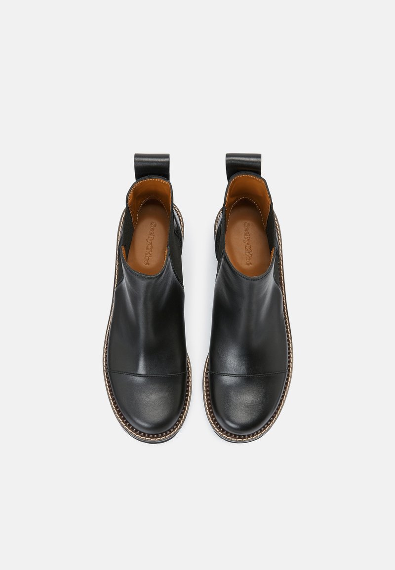 Une paire de bottes Chelsea en cuir noir avec des coutures brunes et des languettes, vue de dessus sur un fond blanc.