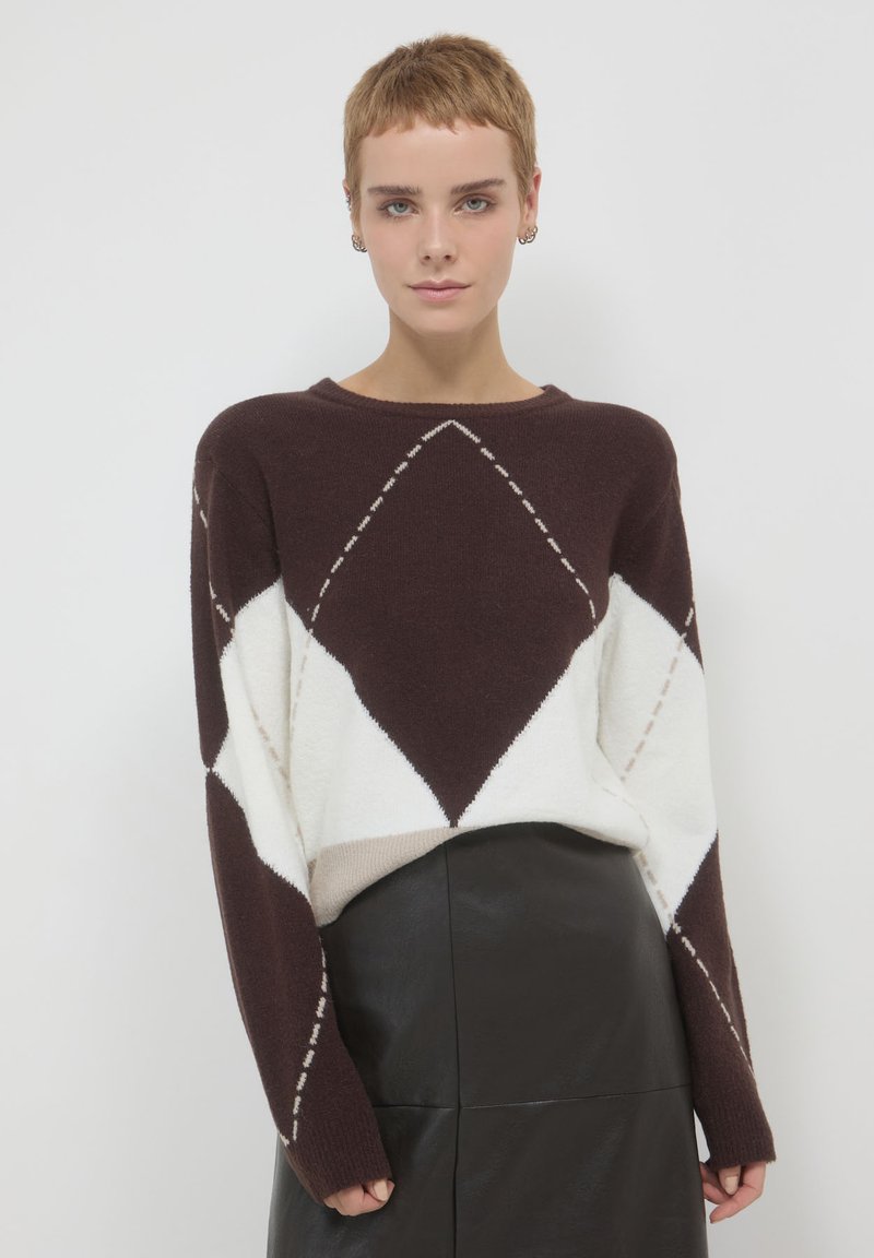 Maglione marrone e bianco con motivo argyle, maniche lunghe, scollatura a girocollo e una texture morbida, abbinato a una gonna in pelle nera.