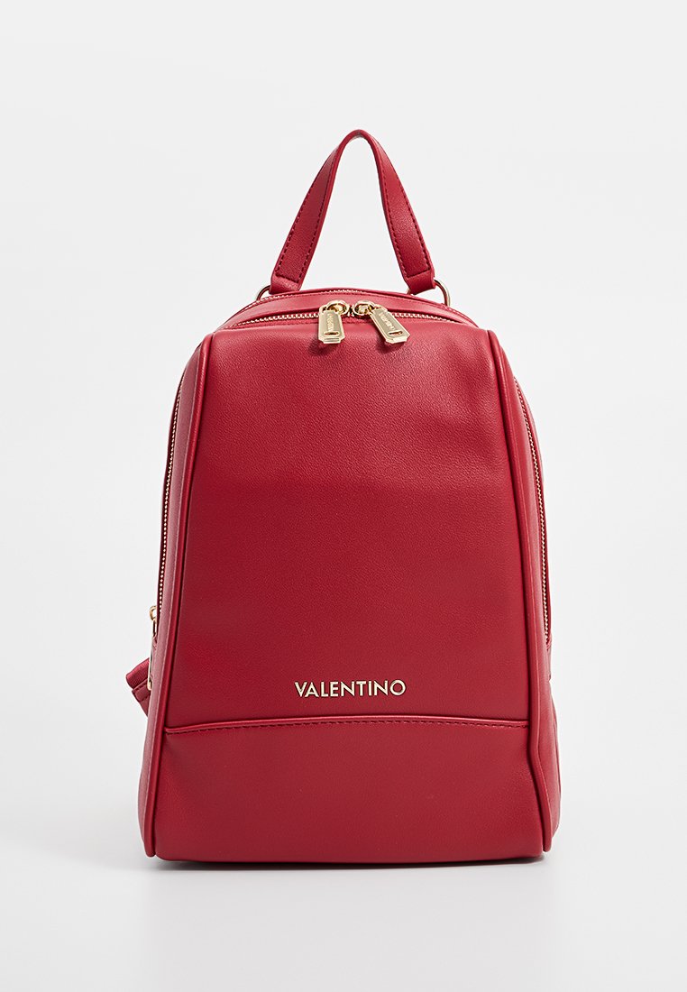 Mochila de cuero rojo con una forma estructurada, cremalleras doradas y un asa superior. Presenta un logo frontal y una textura suave.