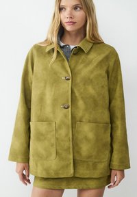 Oliwkowa skórzana kurtka z dwoma przednimi kieszeniami, gładka i przyjemna w dotyku, z zapięciem na guziki. Posiada kołnierz oraz widoczne detale szwu.