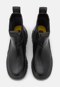Paire de bottines en cuir noir avec languettes et semelles intérieures jaunes, vues de dessus sur fond blanc.