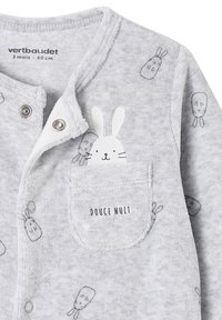 Hellgrau Babystrampler mit kleinen Hasengesichtern, Druckknöpfen, einer Tasche mit der Aufschrift "DOUCE NUIT" und einem weißen Hasen, der aus der Tasche schaut.