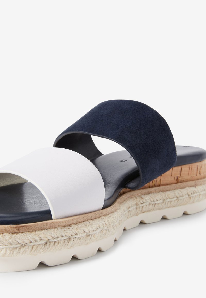 Twee-kleurige slippers met een bovenwerk van wit leer en een marineblauwe suède band. Dikke zool met jute-details en een gestructureerde rubberen basis.