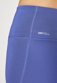 Lilla treningsleggins med en jevn tekstur, med høyt liv og kontrasterende sømmer. "DRYCELL"-logoen er plassert på siden.