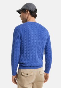 Blauwe kabelgebreide trui van zacht materiaal, met een ronde hals, geribde manchetten en zoom. Gepaard met beige broeken met zakken.