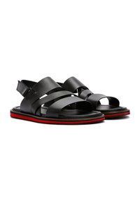 Zwarte leren sandalen met meerdere brede banden en open tenen. Beschikt over een gestructureerde zool met een contrasterende rode streep langs de rand.