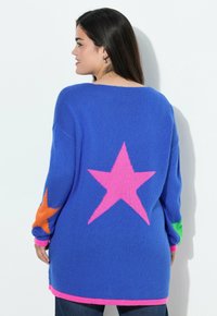 Maglione blu lavorato a maglia con grandi stelle rosa e arancioni sul retro e sulle maniche, con orlo e polsini ribattuti rosa.