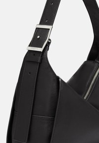 Czarna skórzana torba na ramię o teksturowanym wykończeniu, z metalową klamrą i zamkiem błyskawicznym po boku.