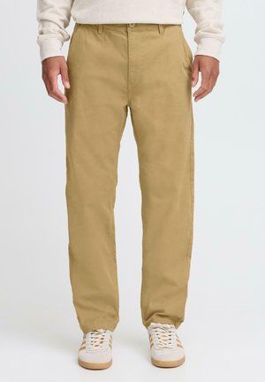 Khaki cotton trousers with a straight cut, front pockets, and a flat closure. Paired with white sneakers featuring beige accents.