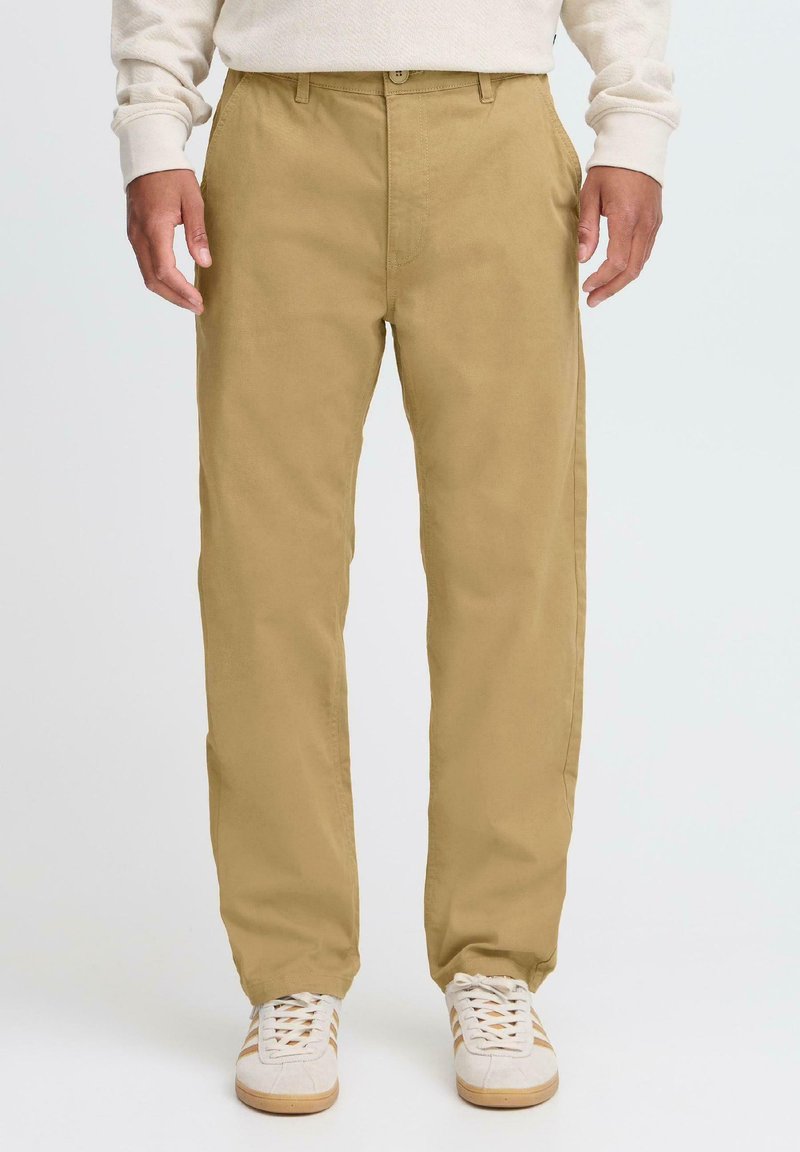 Khaki cotton trousers with a straight cut, front pockets, and a flat closure. Paired with white sneakers featuring beige accents.