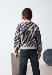 Fuzzy sweater in soft pink with dark zebra stripes, high neck, drop shoulders, paired with dark gray wide-leg jeans, minimalistic background.