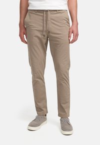 Beige, lette bukser med snor i livet, smal passform, sidelommer og glat overflade, parret med grå ruskindssko.
