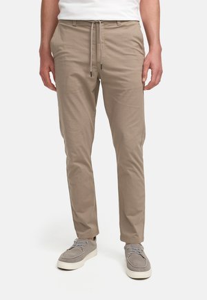 Beige, lette bukser med snor i livet, smal passform, sidelommer og glat overflade, parret med grå ruskindssko.