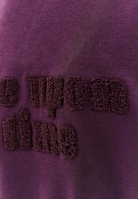 Fialová bavlněná látka s texturou, na které je vyšitá fuzzy fráze "Kdysi dávno" v mírně tmavším odstínu fialové.