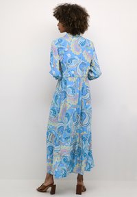 Dolga modra obleka s paisley vzorcem v pastelnem barvnem spektru, z večplastno zasnovo in zavihanimi rokavi, izdelana iz lahkega, tekočega materiala.
