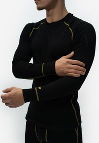 Zwarte lange mouwen shirt met gele stiksels. Rekbare stof, aansluitend ontwerp, ribbelmanchetten en een subtiele logo op de pols.