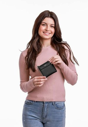 Černá peněženka na zip držena v jedné ruce, s jednoduchým designem, hladkým povrchem a jemným logem na přední straně; modelka má na sobě růžový žebrovaný svetr.