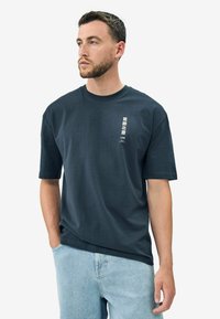 Dark navy cotton t-shirt with short sleeves, round neckline, and small white graphic print on the left side. Casual fit and soft texture.