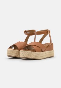 Sandalete platform din piele ecologică maronii, cu bretele crisscross, cataramă la gleznă și detalii din iută împletită pe talpa wedge.